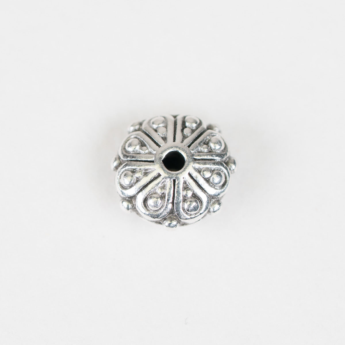 A single round silver-toned metal bead with an ornate floral or sunburst pattern and a small black center hole, shown on a plain white background.