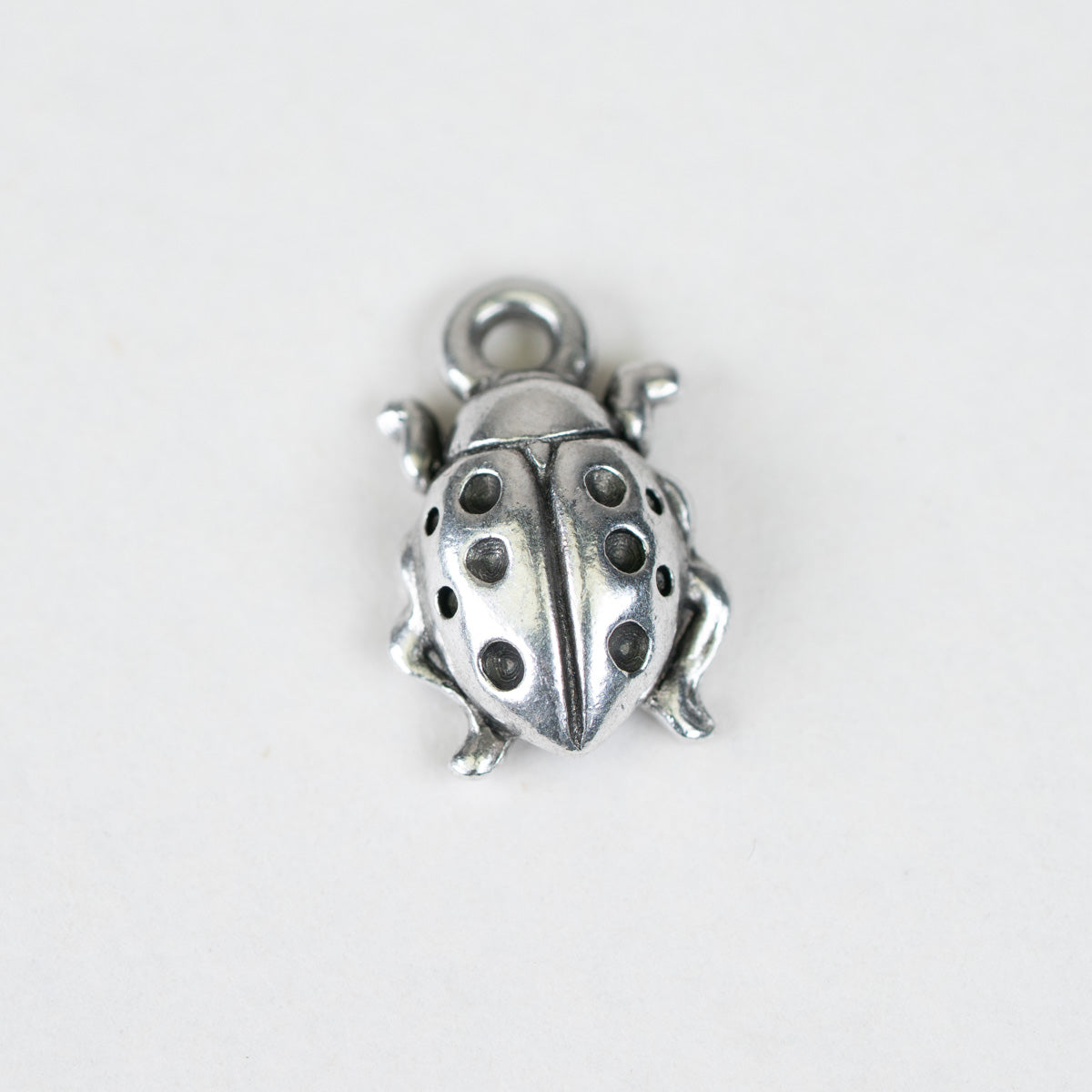 A small metallic ladybug charm with a silver-toned finish and dark oxidized spots, shown on a plain light background.