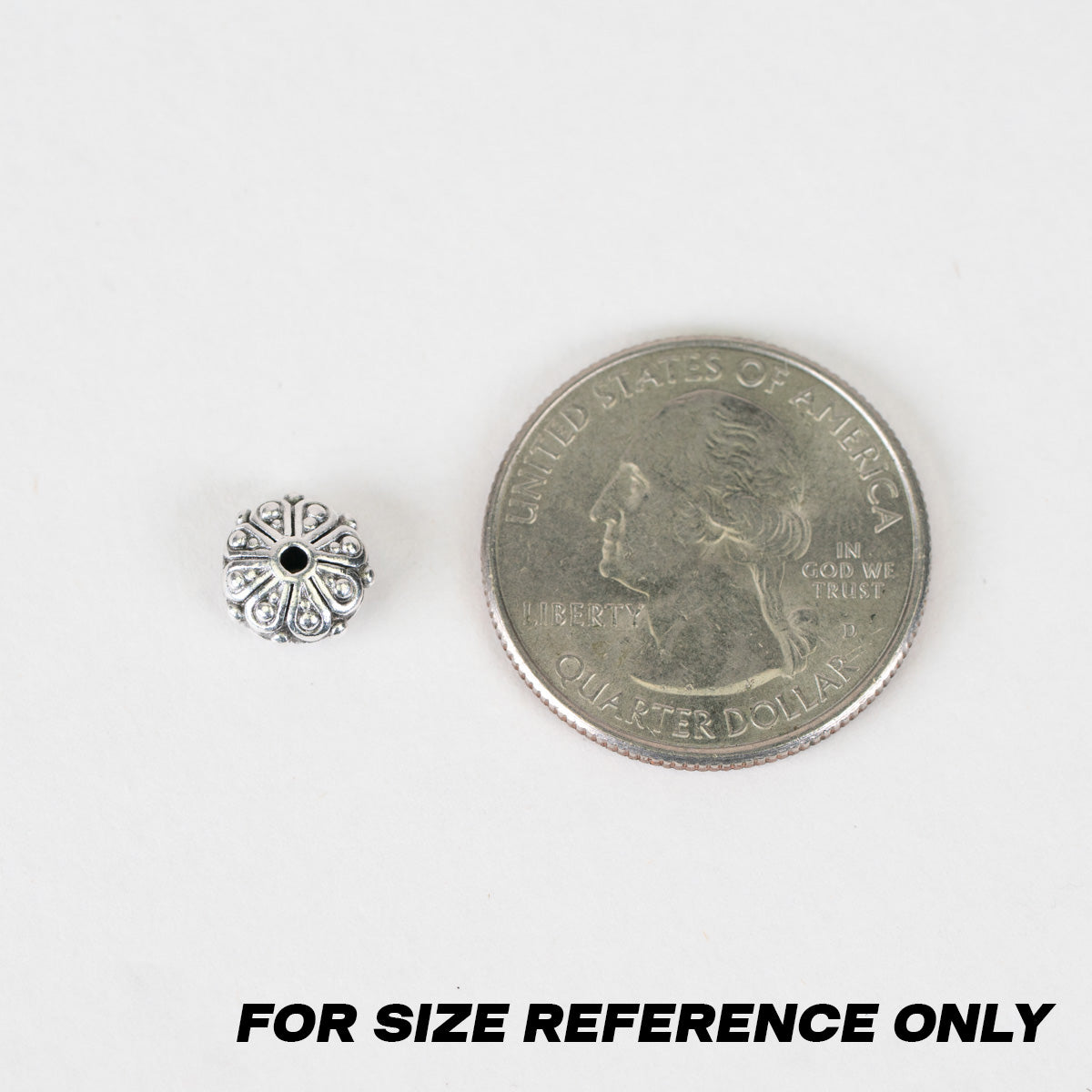 A small silver-toned decorative bead shown next to a U.S. quarter