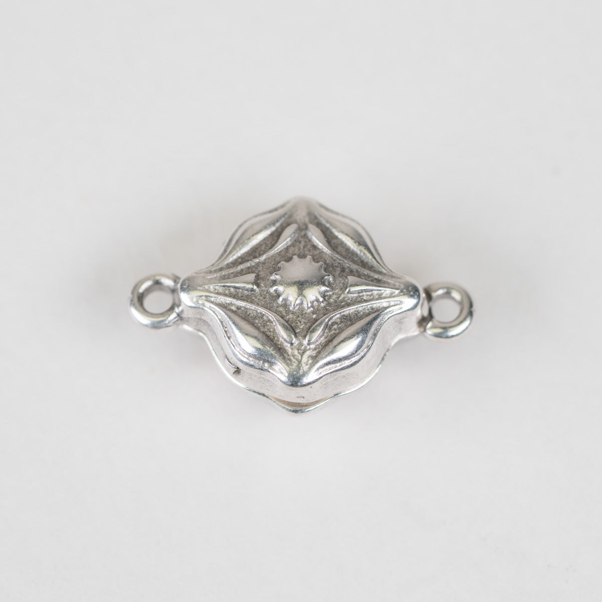 A small silver-toned metal jewelry connector charm with a decorative textured center and two loops on the sides, shown on a plain light background.