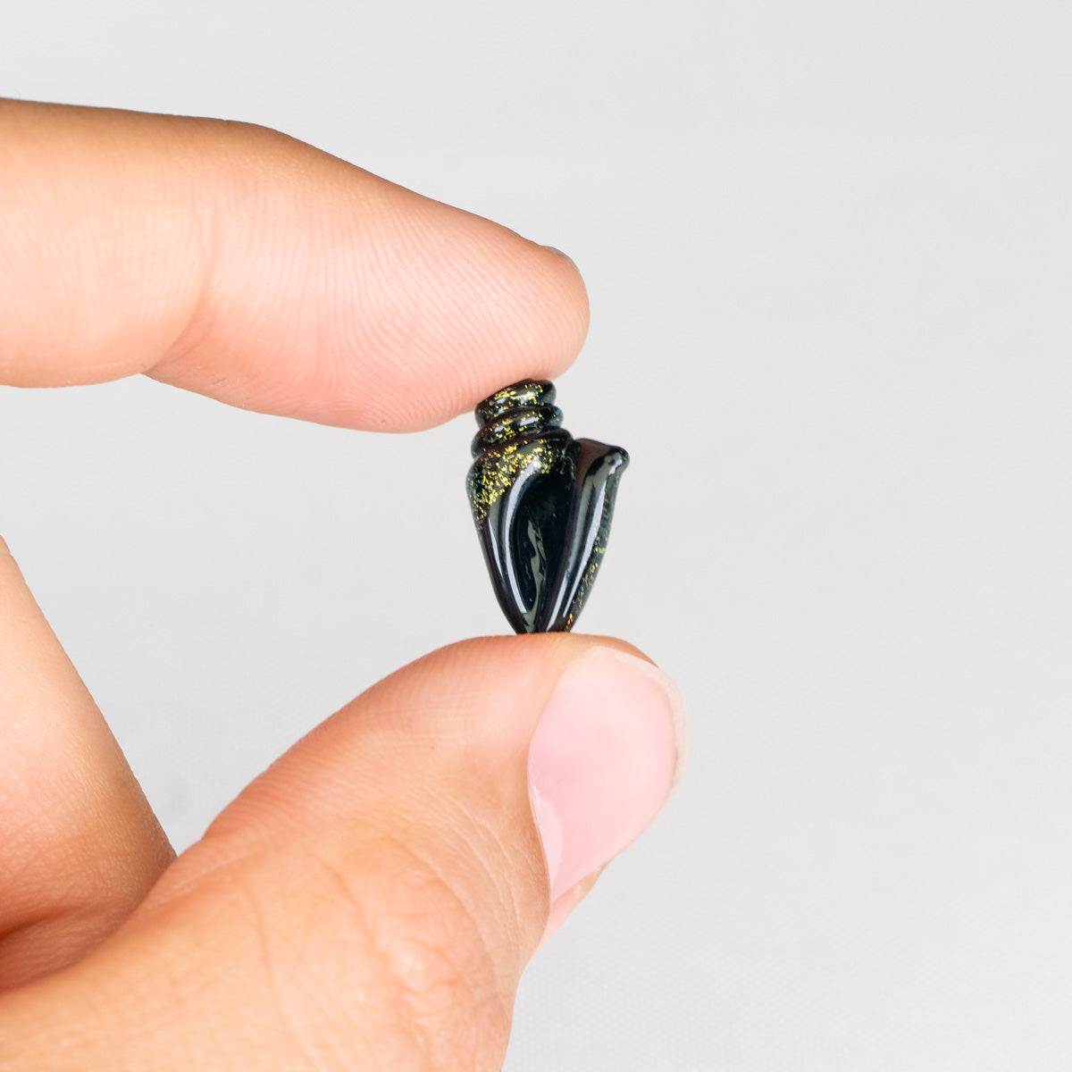 Small black seashell glass bead held between two fingers against a light white background