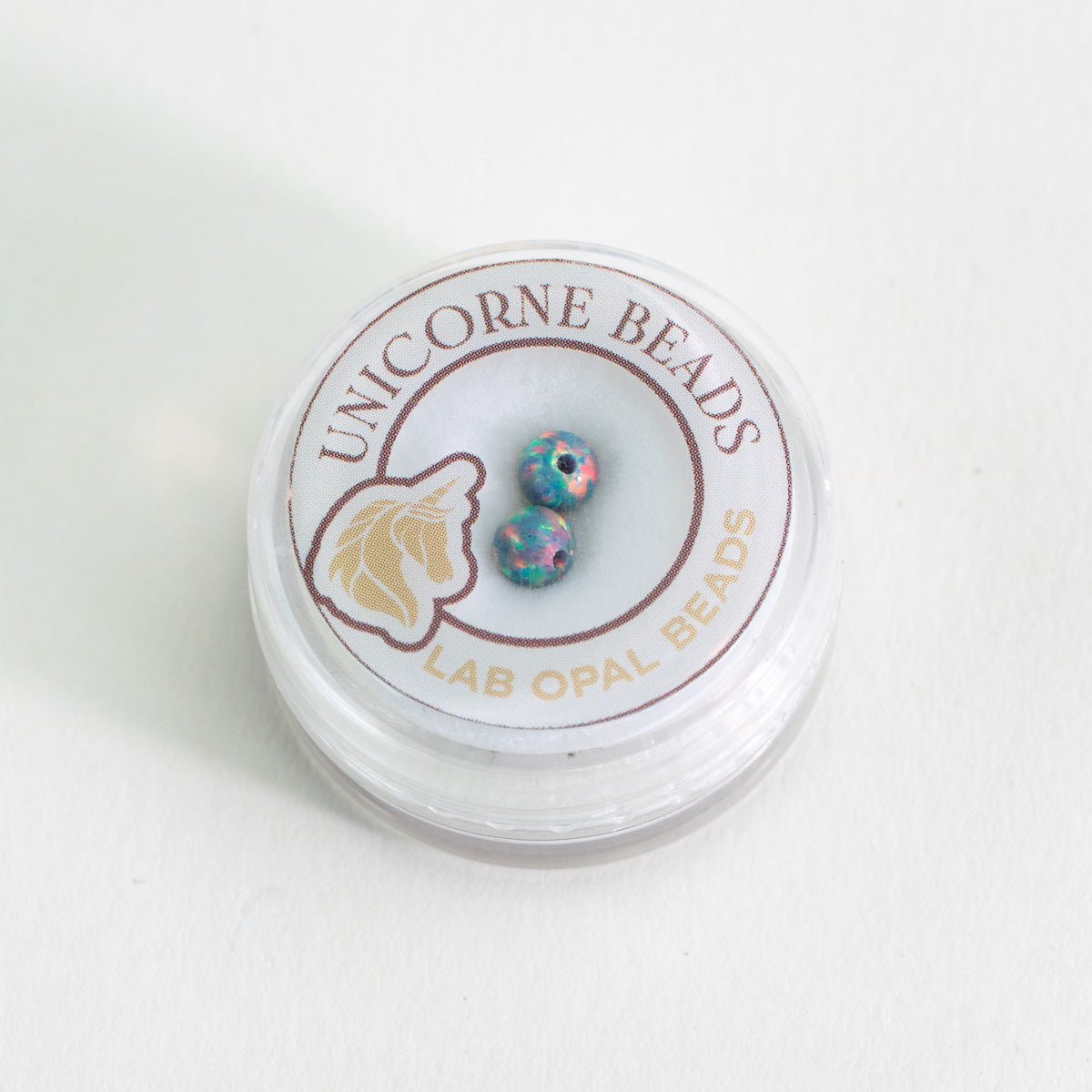 Unicorne Beads container with lab opal beads on a white background