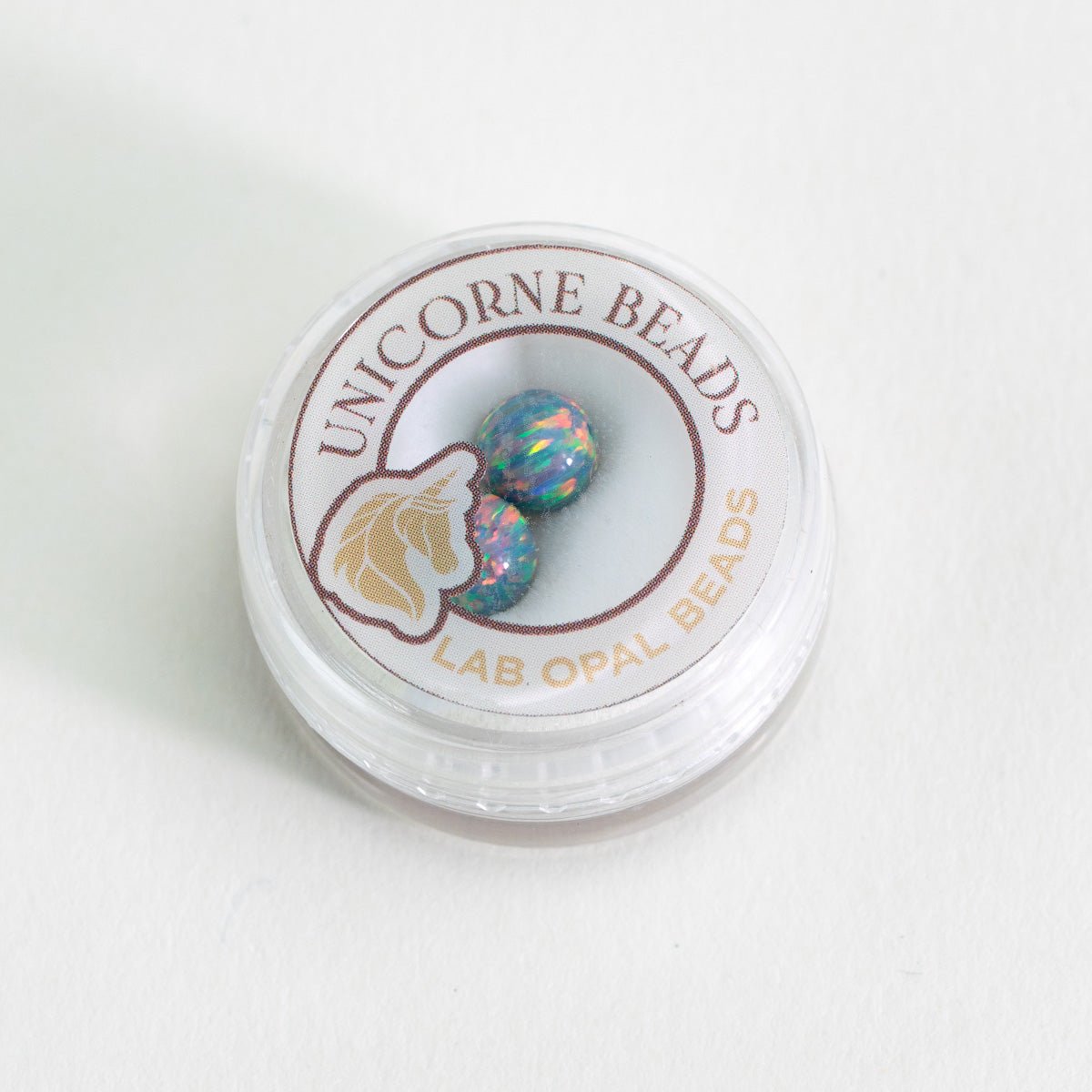 Container of Unicorne Beads with lab opal beads on a white background