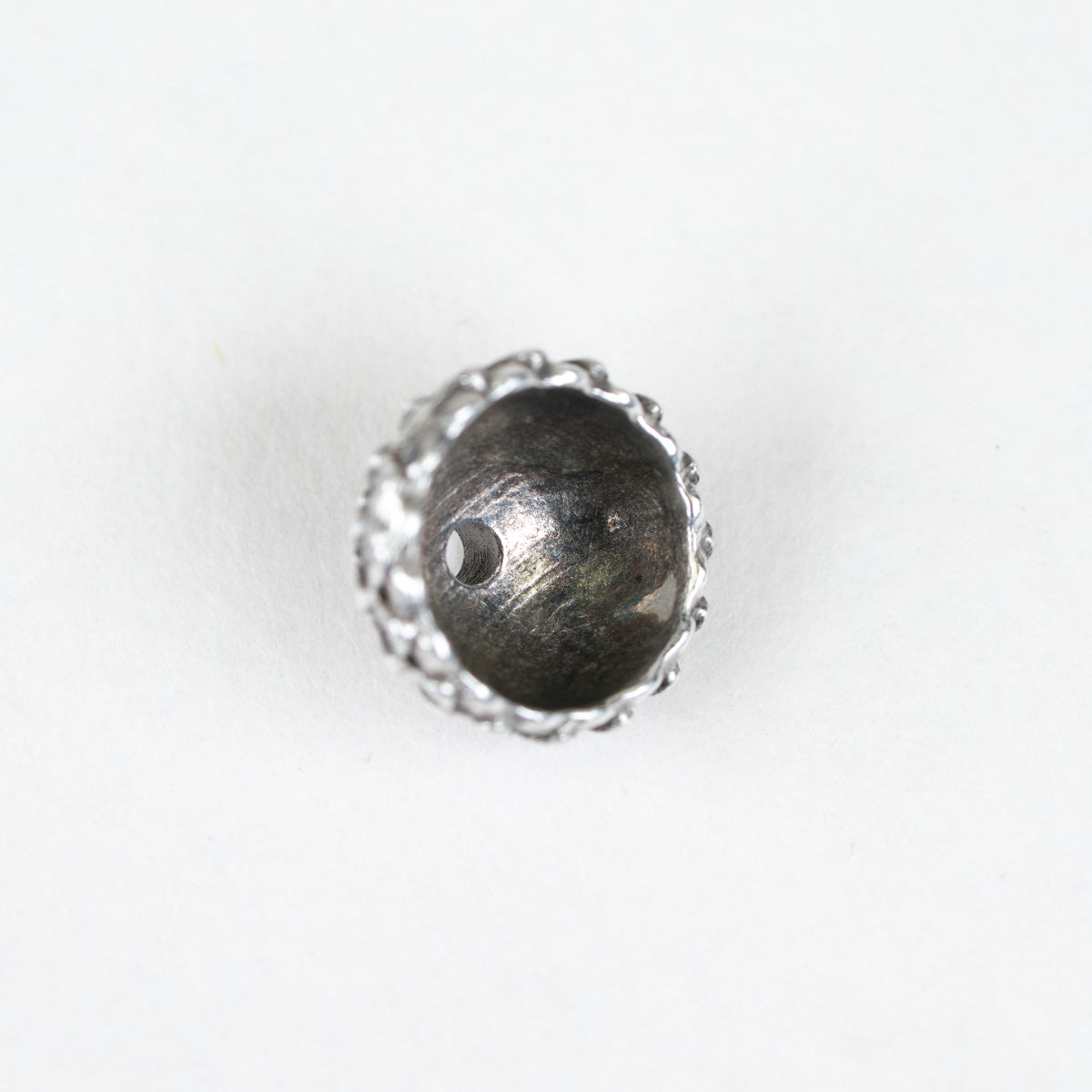 A single silver-toned metal bead with a textured, scalloped outer edge and a smooth, dark metallic interior, shown on a plain white background.