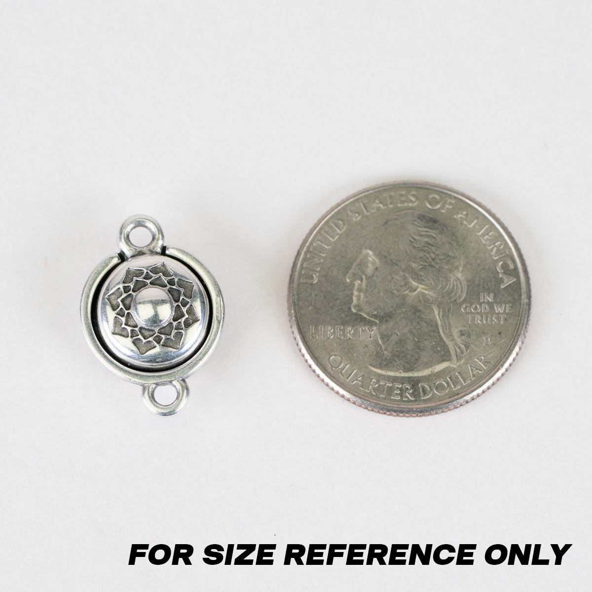 A silver-toned metal round charm with a floral pattern and two hanging loops, shown next to a U.S. quarter
