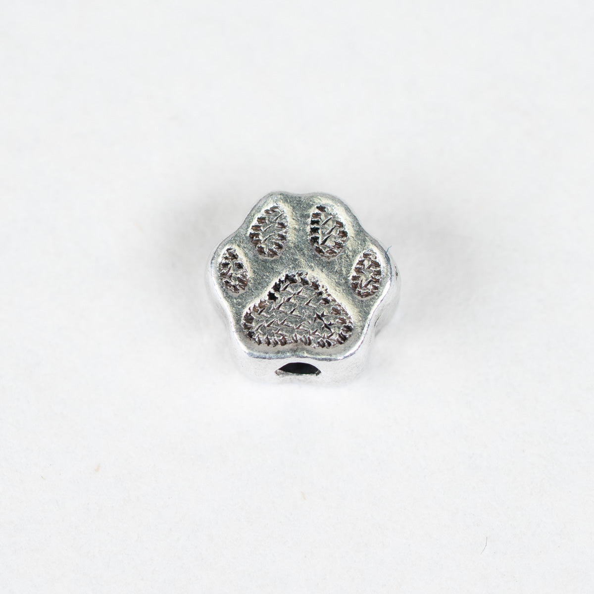 A small silver-toned metal charm shaped like a paw print, shown on a plain white background.