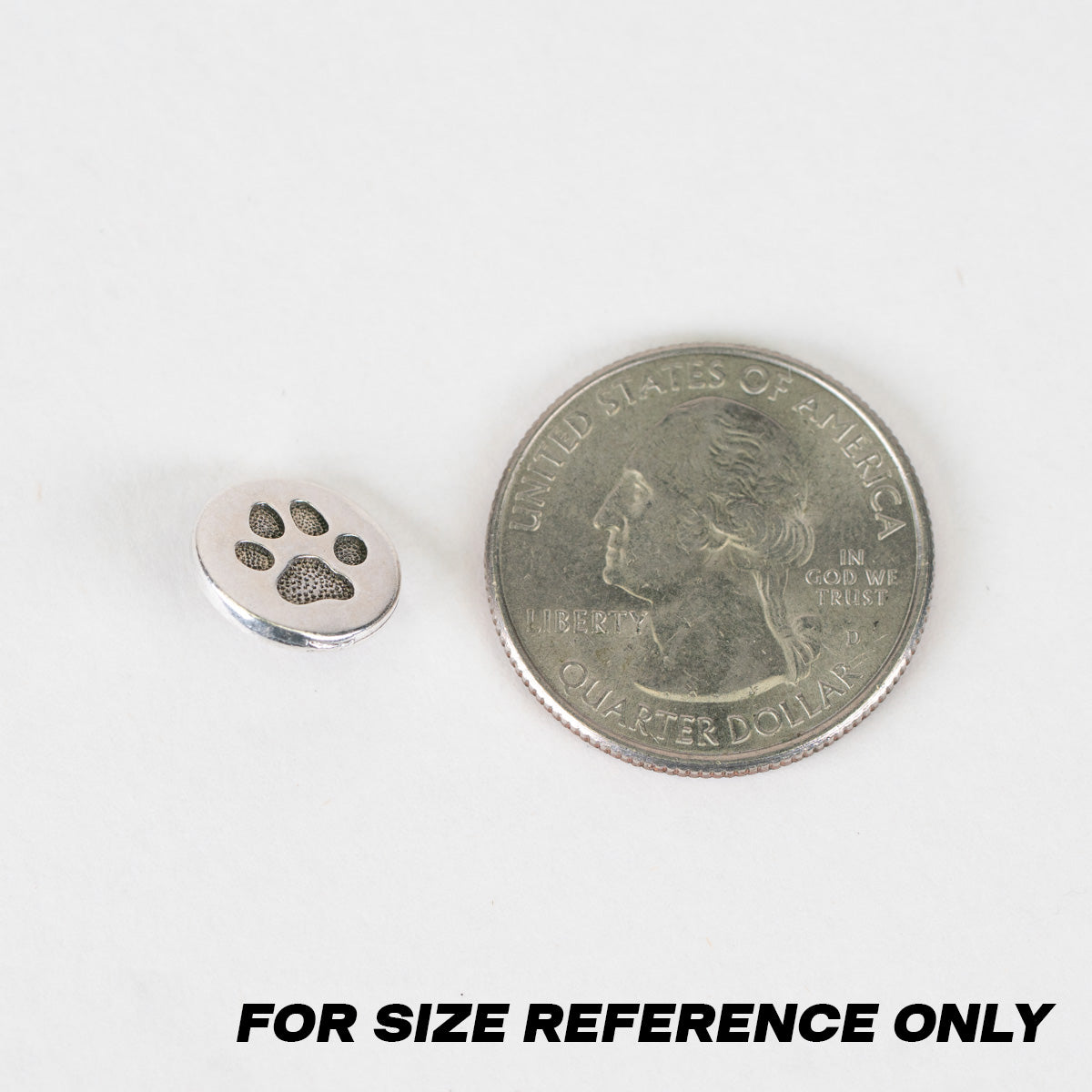 A small silver metal charm shaped like a paw print shown next to a U.S. quarter