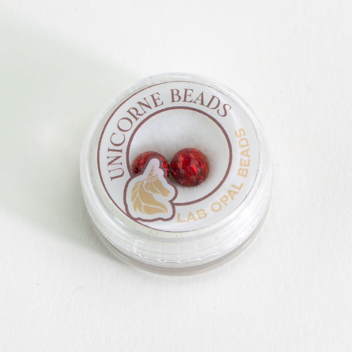 Container of red cherry beads in packaging with tan unicorn