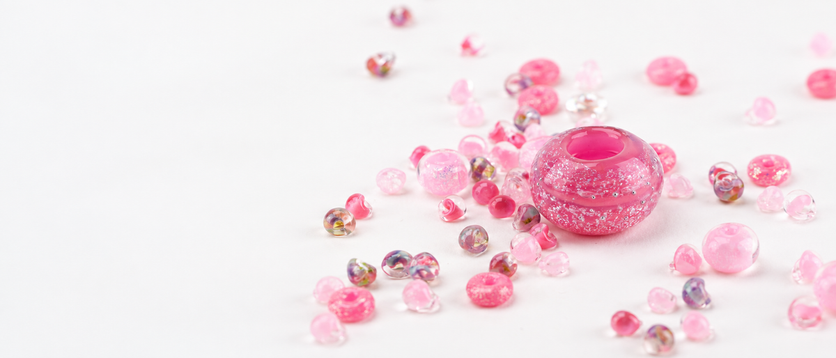 Handmade pink glass beads arranged on a white background for the Unicorne Beads Breast Cancer Awareness collection.