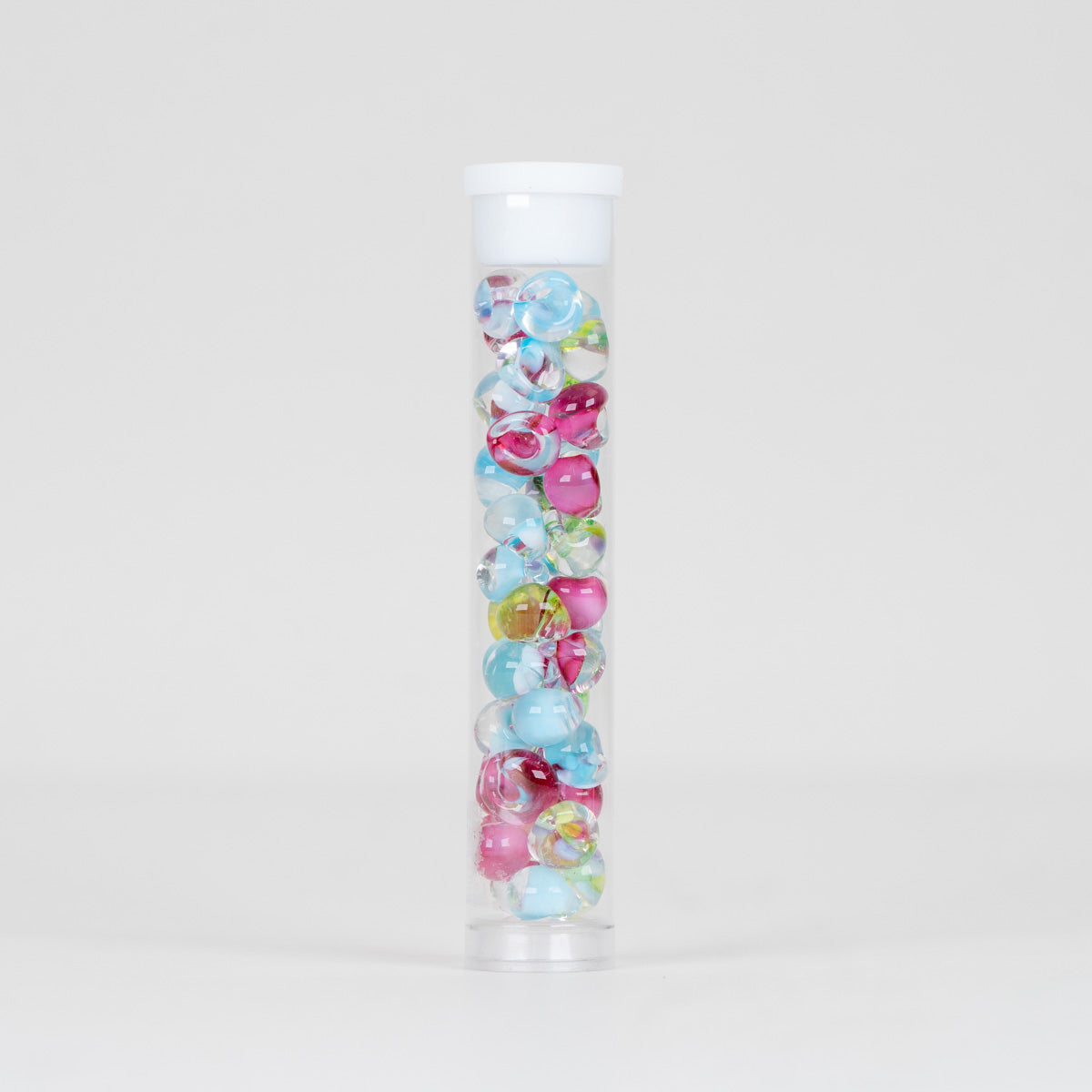 Pink, blue, and green beads in a clear miniature tube on a plain white background