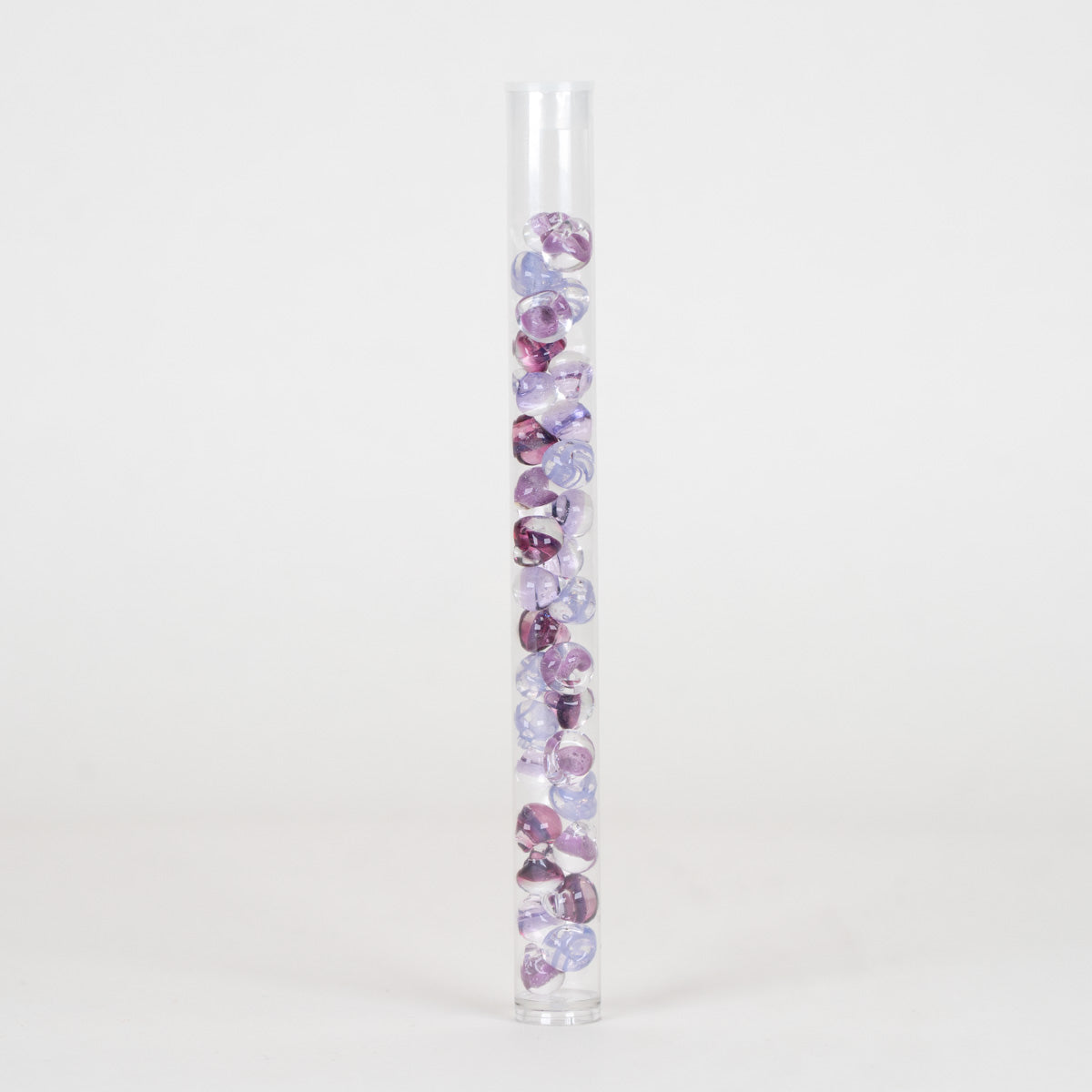 A clear cylindrical tube filled with small round purple and lavender decorative beads, photographed against a plain light gray studio background.