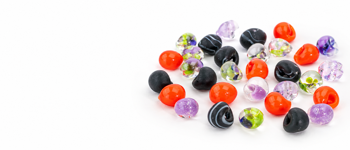 Colorful Halloween glass beads in orange, black, purple, and green displayed on a white background for Unicorne Beads' 25% off Halloween sale.