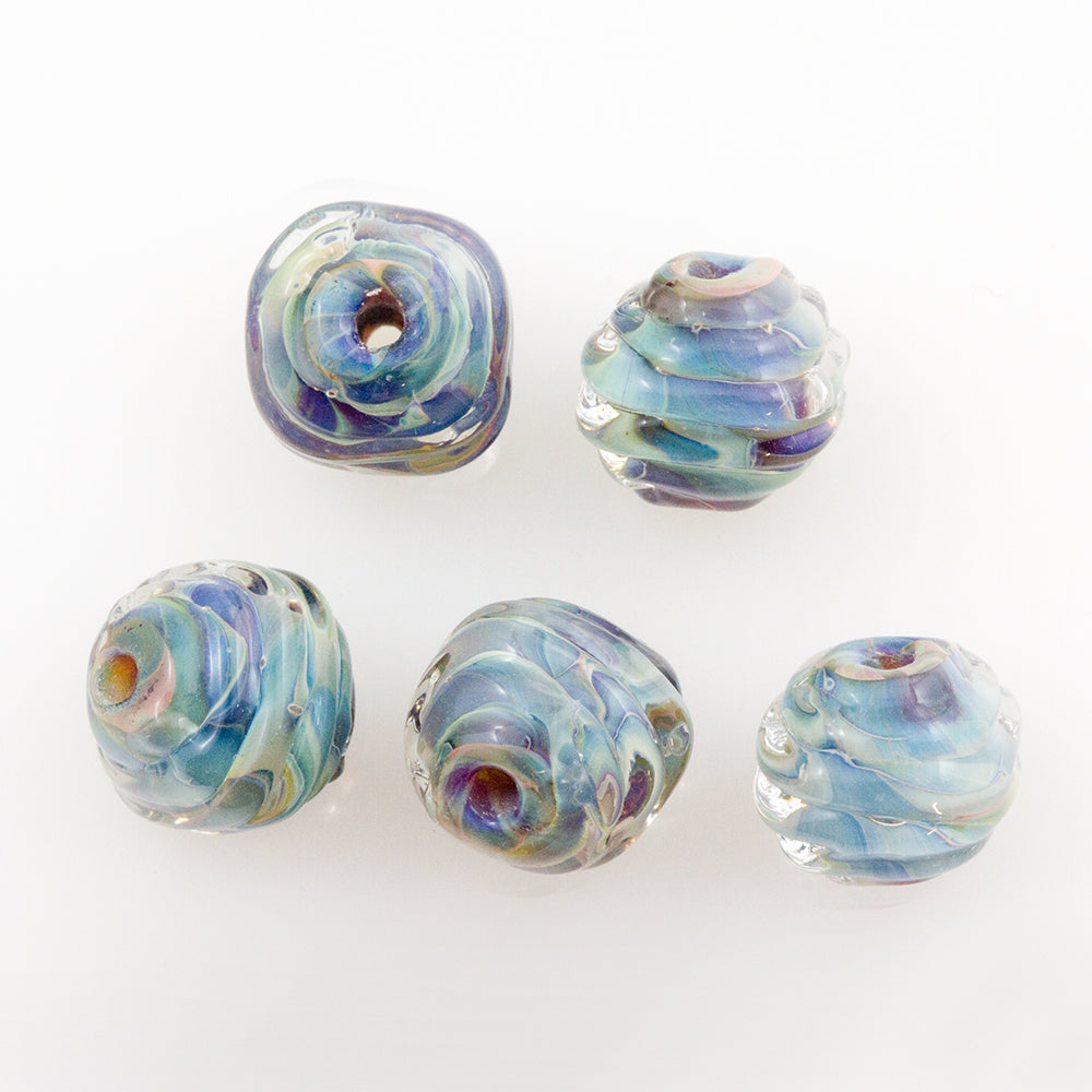 Five coconut shape glass jewelry beads used to make jewelry. Each glass bead is blue, purple, and green and features a hole to be used by jewelry makers to string on pieces.
