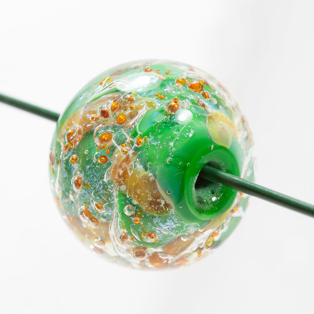 Green donut bead on a string, with copper globs embedded throughout. The glass bead has a hole through the center to be used for jewelry making. 