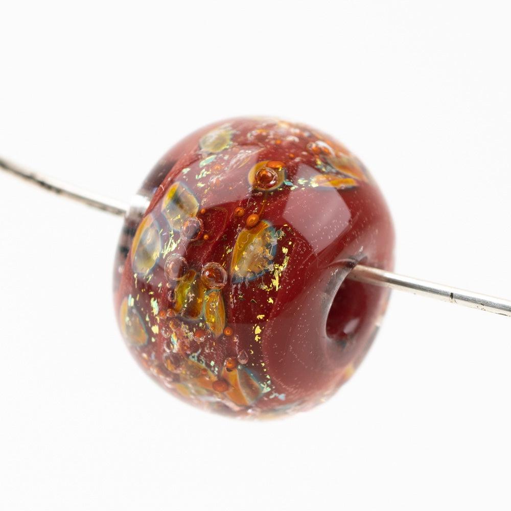 A single red and orange glass bead sitting on a metal wire. The glass bead has a center hole used for jewelry making. 