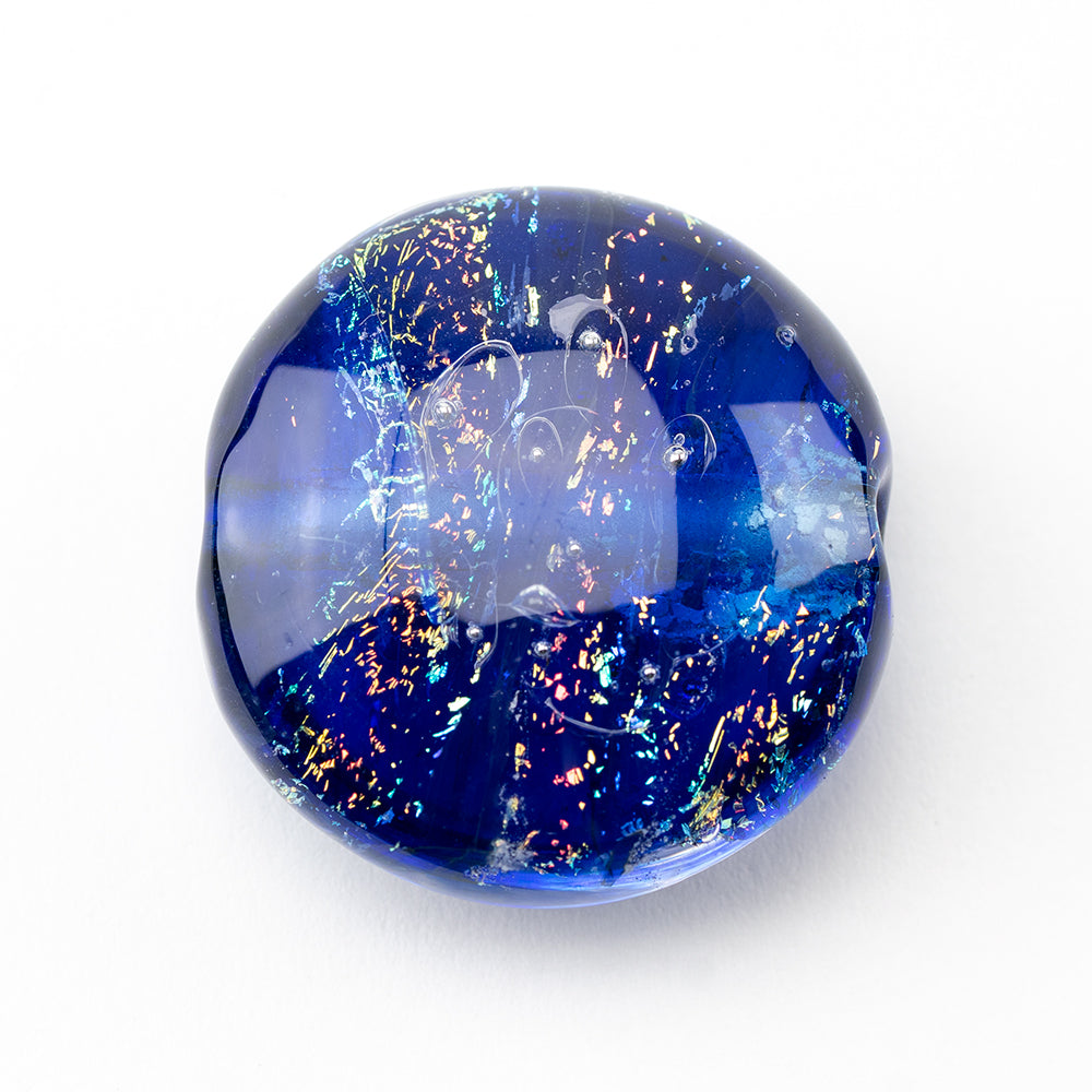 One large glass bead, dark blue in color with dichroic, rainbow foiling. The bead has two holes that go through the glass bead to be used in jewelry craft.