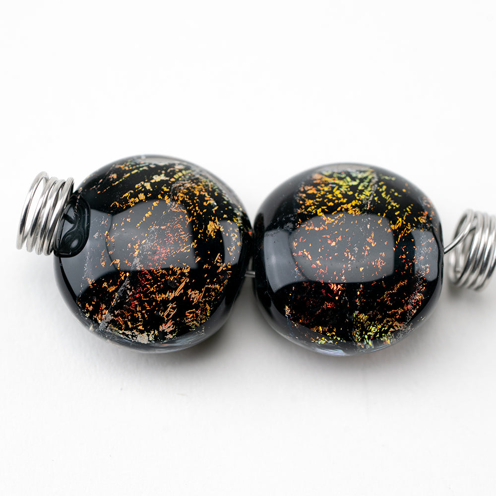Two glass beads from Unicorne Beads, black in color with a rainbow display of dichroic accents. Each bead is hollow to be used for jewelry works.