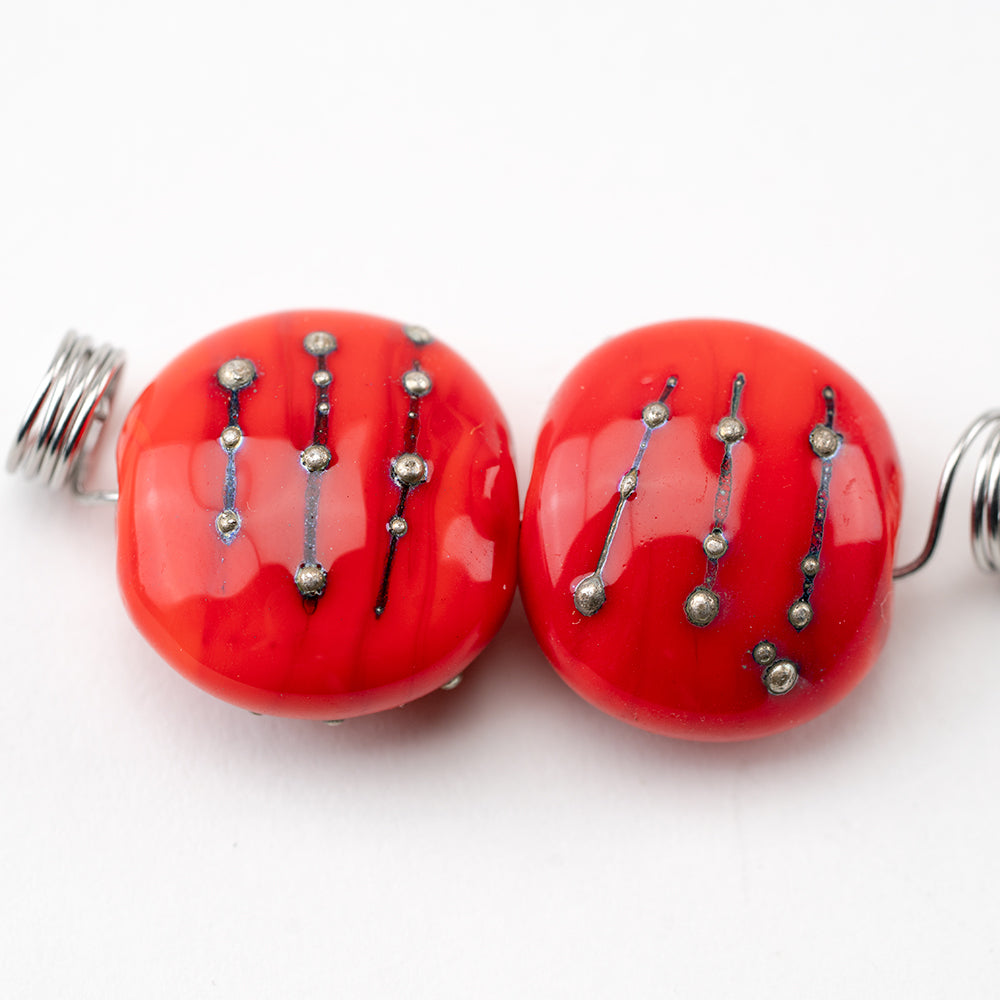 Two red glass beads made for jewelry making. Glass beads feature silver beading and a hollow center to be used for jewelry projects. 