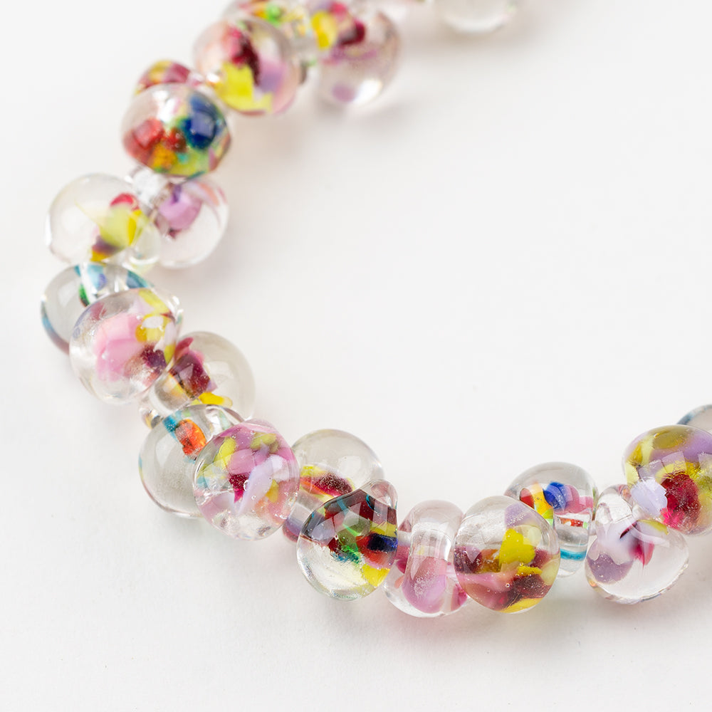 A strand of Portofino Teardrop glass beads crafted by Unicorne Beads. These glass beads are shaped like teardrops and are multicolored with a clear base. Each glass bead has a hole in the middle to be used for jewelry craft projects.