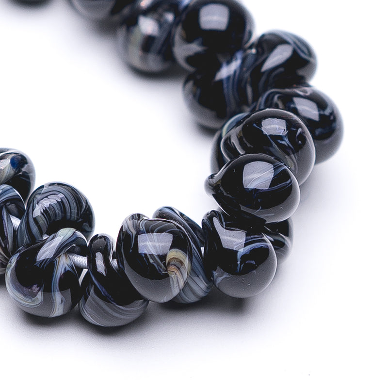 A strand of Black Dahlia Teardrop beads crafted by Unicorne Beads. These Beads are shaped like teardrops and are black with blue accent swirls. Each bead has a hole in the middle to be used for jewelry craft projects.
