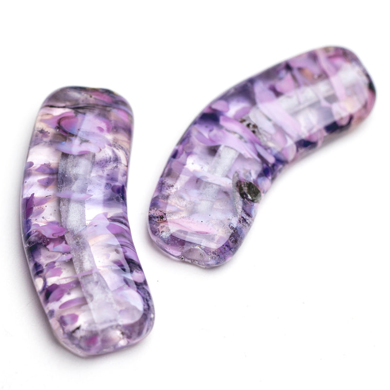 A pair of banana-shaped beads with a flat top and bottom. Color of beads is a vibrant purple, clear, and black. Beads include holes in each side used to put string through for jewelry making.